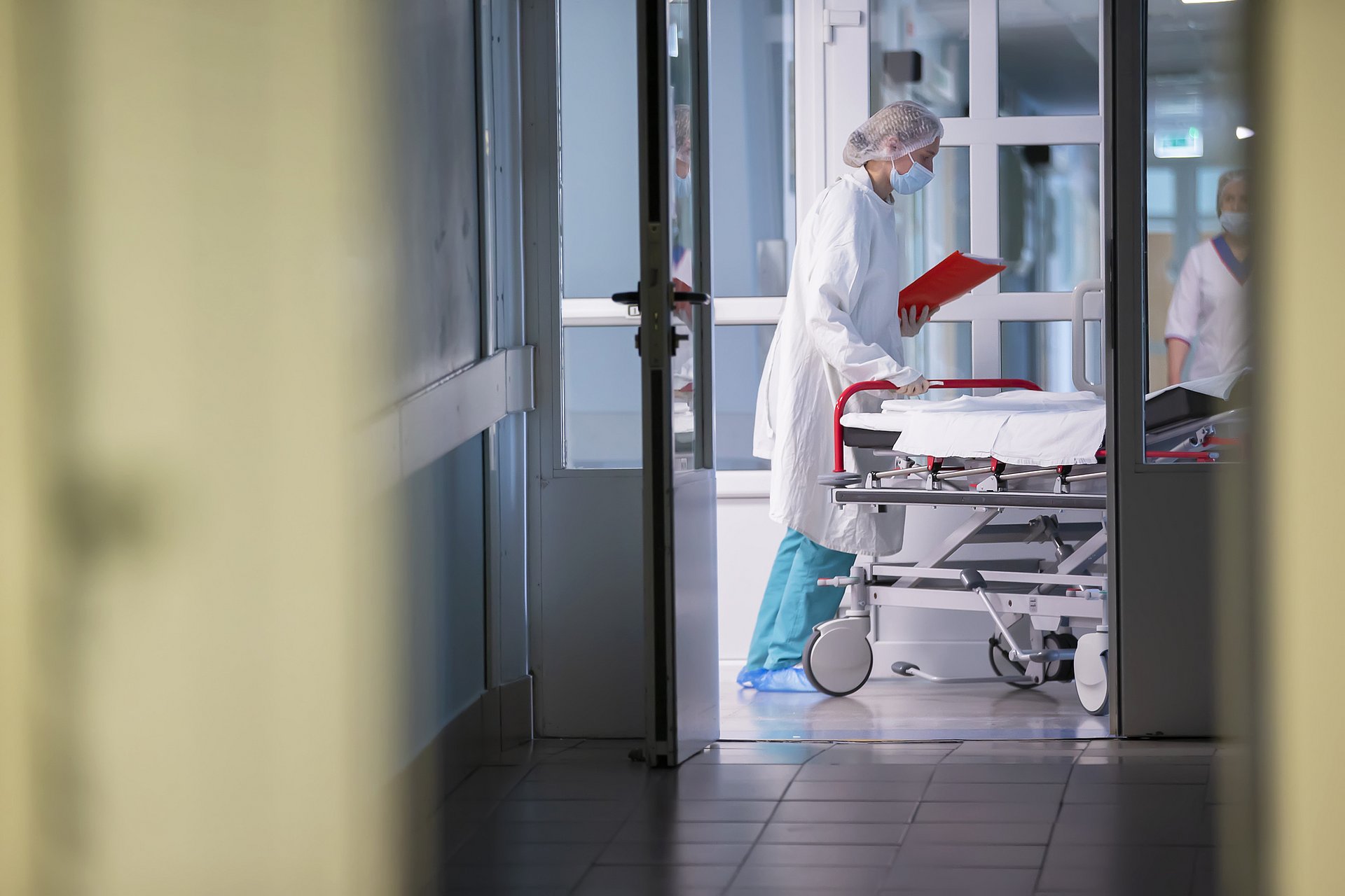 A hospital bed is pushed across a hospital corridor. 