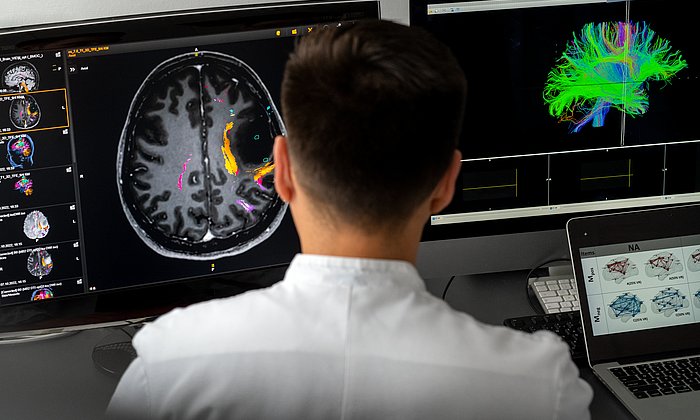 Forscher sitzt vor zwei Bildschirmen und macht eine 