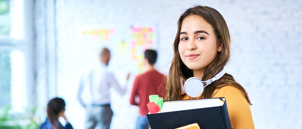 Female student looking into the camera, in the background a bright, modern seminar room