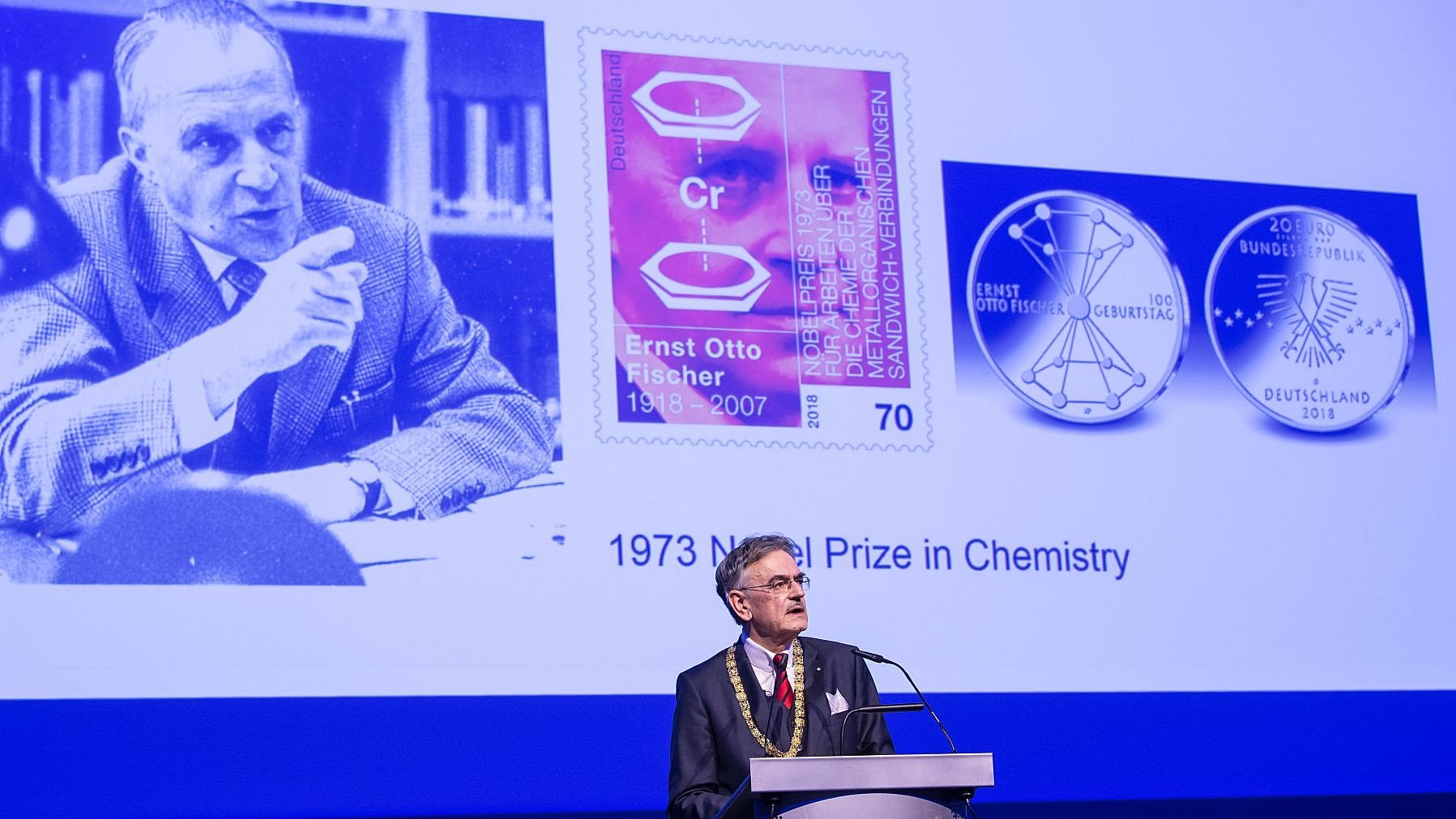 President Emeritus Wolfgang A. Herrmann, acting TUM President in the anniversary year 2018, gives a speech at the annual academic celebration “Dies Academicus” in 2018. In the background, a presentation with photos of Nobel Prize winner Ernst Otto Fischer can be seen.