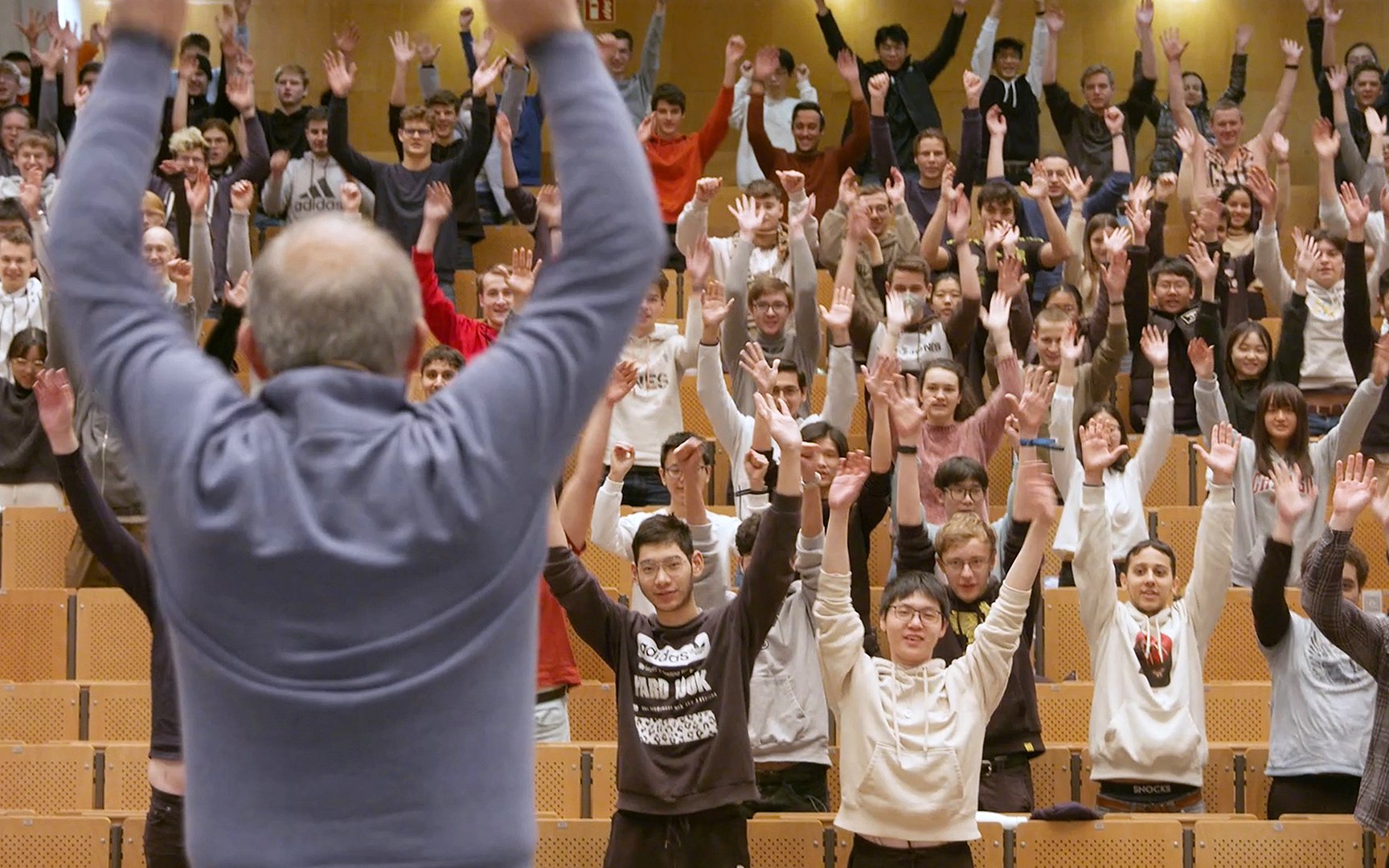 Activity break during the lecture: Prof. Diepold can be seen in the lecture hall from behind, stretching his arms upwards, students in front of him, also with their arms stretched upwards