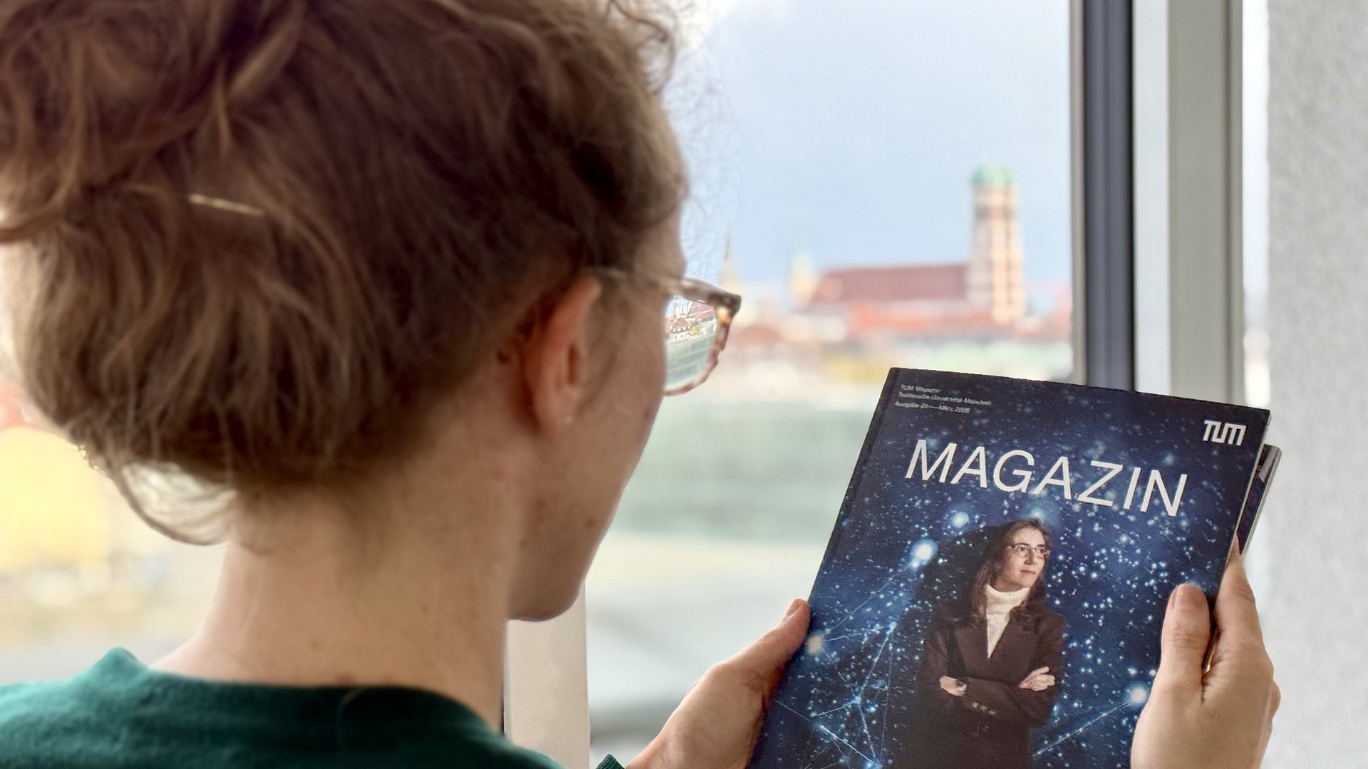Eine Frau hält eine Ausgabe des TUM Magazins in der Hand, im Hintergrund ist die Frauenkirche zu sehen.