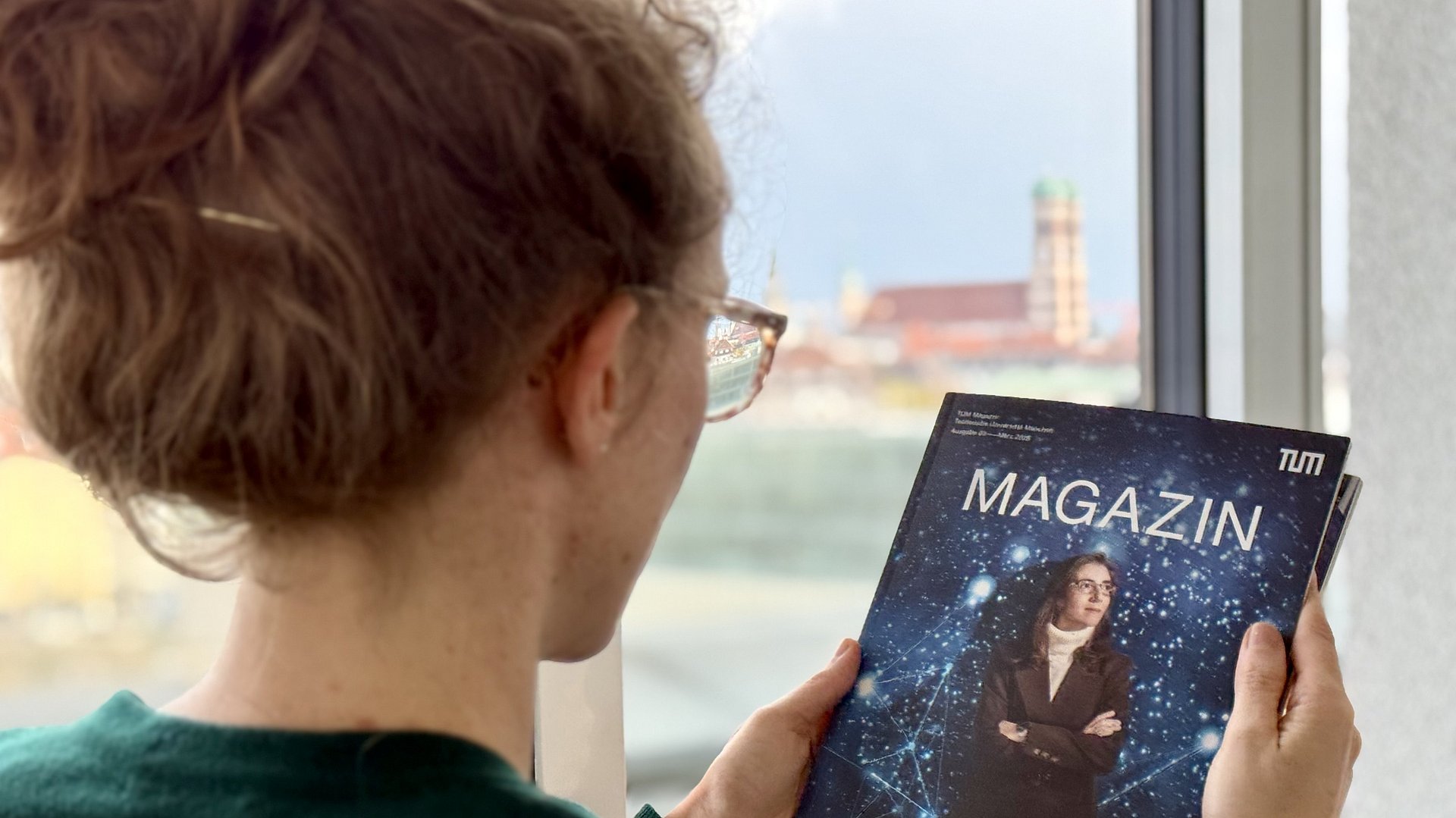 A woman is reading an issue of TUM Magazine, with the Frauenkirche visible in the background.