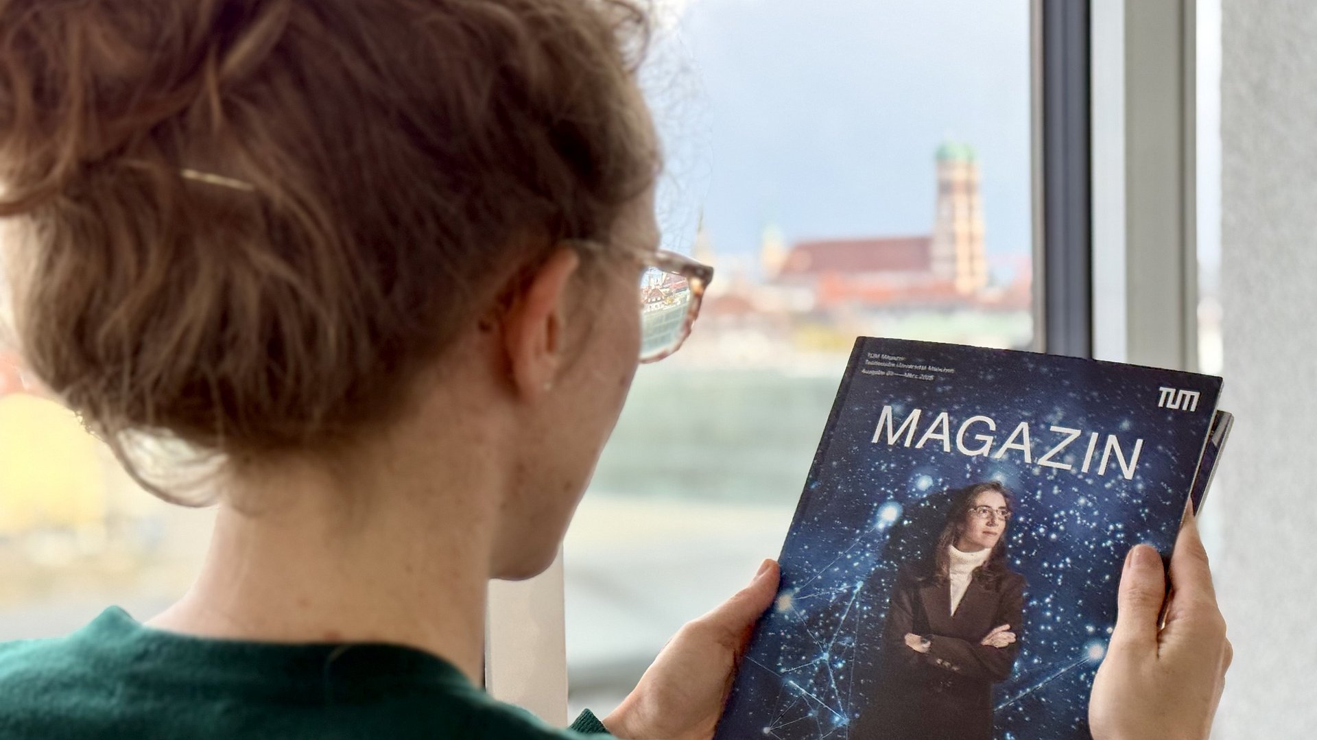 Eine Frau hält eine Ausgabe des TUM Magazins in der Hand, im Hintergrund ist die Frauenkirche zu sehen.