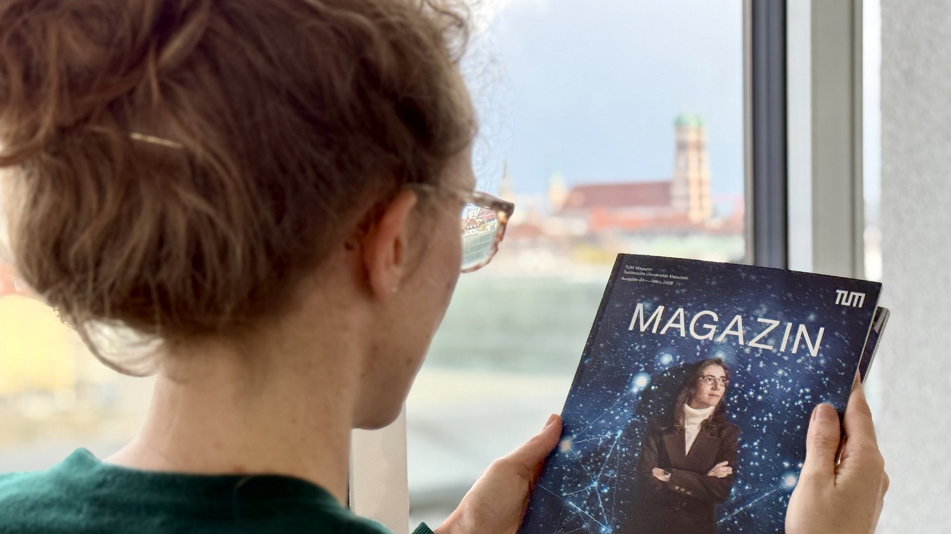 A woman is reading an issue of TUM Magazine, with the Frauenkirche visible in the background.