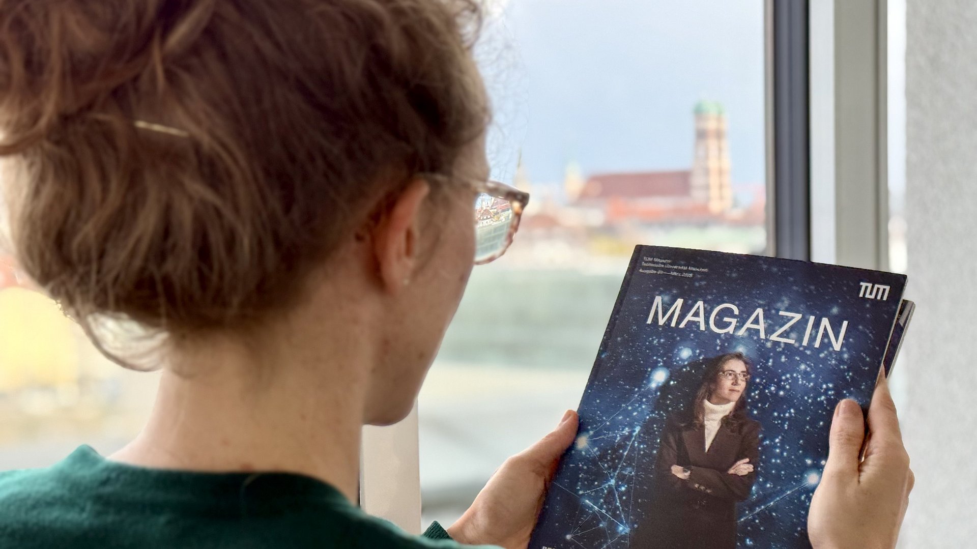 A woman is reading an issue of TUM Magazine, with the Frauenkirche visible in the background.