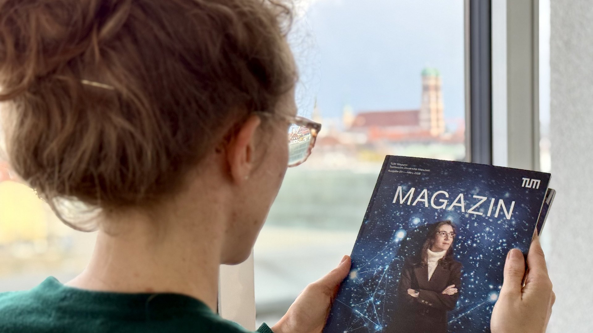 Eine Frau hält eine Ausgabe des TUM Magazins in der Hand, im Hintergrund ist die Frauenkirche zu sehen.