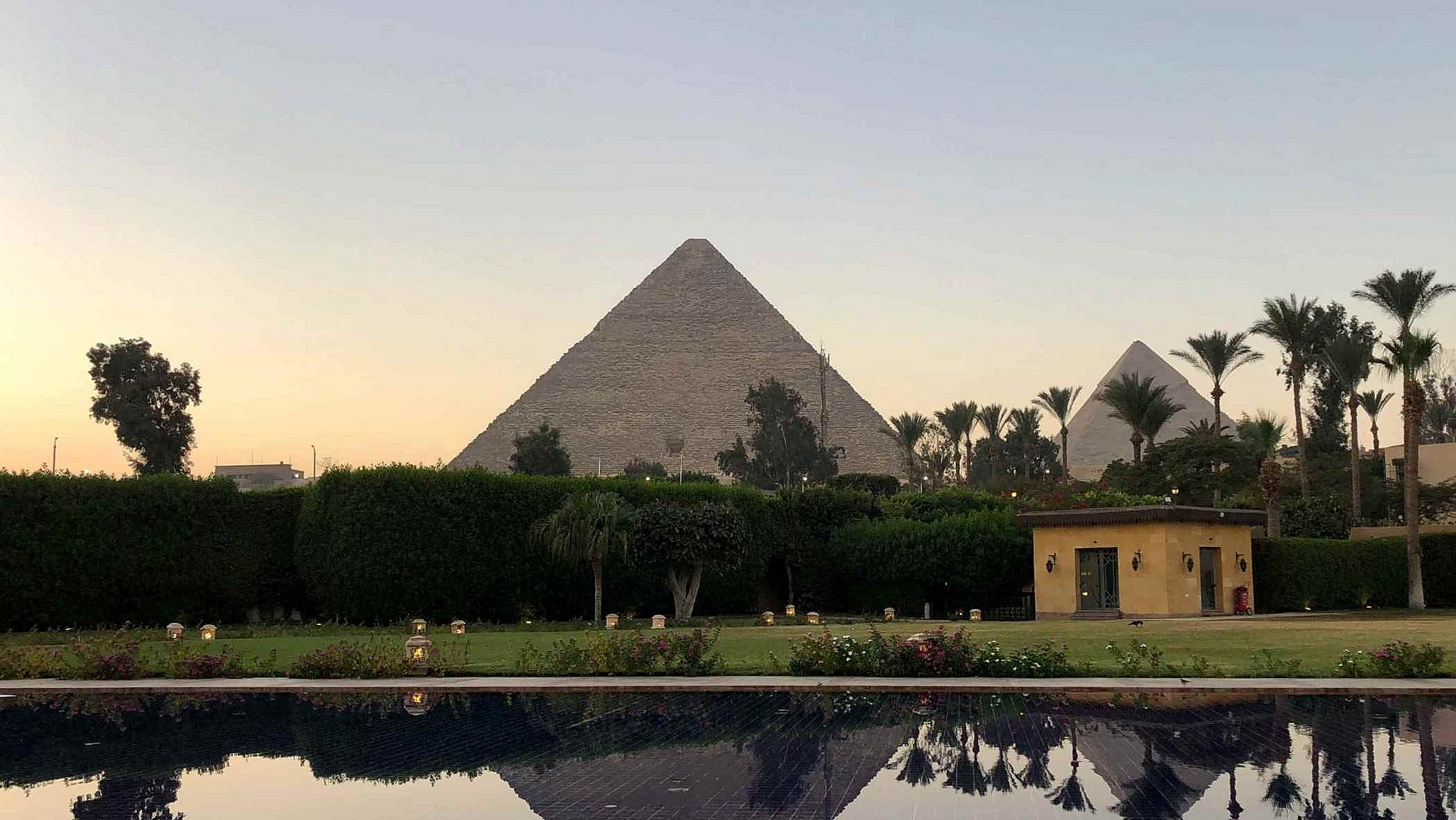 Cheops pyramid from a distance, palm trees and water in the foreground