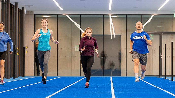 [Translate to English:] Vier Stueirende sprinten in einer der größten neuen Sporthallen.