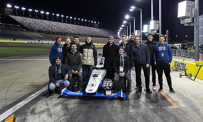 A group of scientists stand around a formula racing car.