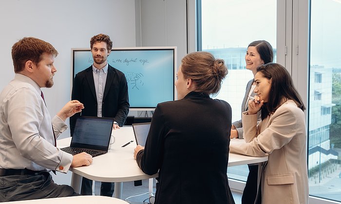 Several people stand around a table in a seminar room and take part in a workshop.