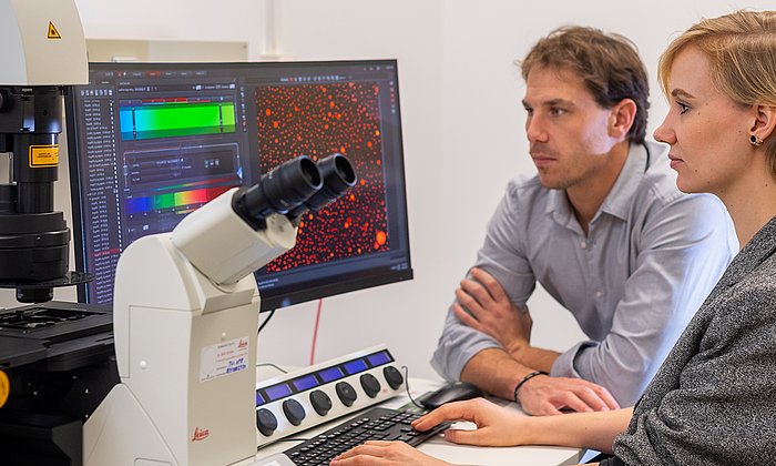 Prof. Job Boekhoven and Caren Wanzke discovered a new material system that can release drugs with a constant release rate over a tunable period of time. The microscopic image (right screen) shows droplets of the hydrolyzable oil-emulsion embedded in a hydrogel. 