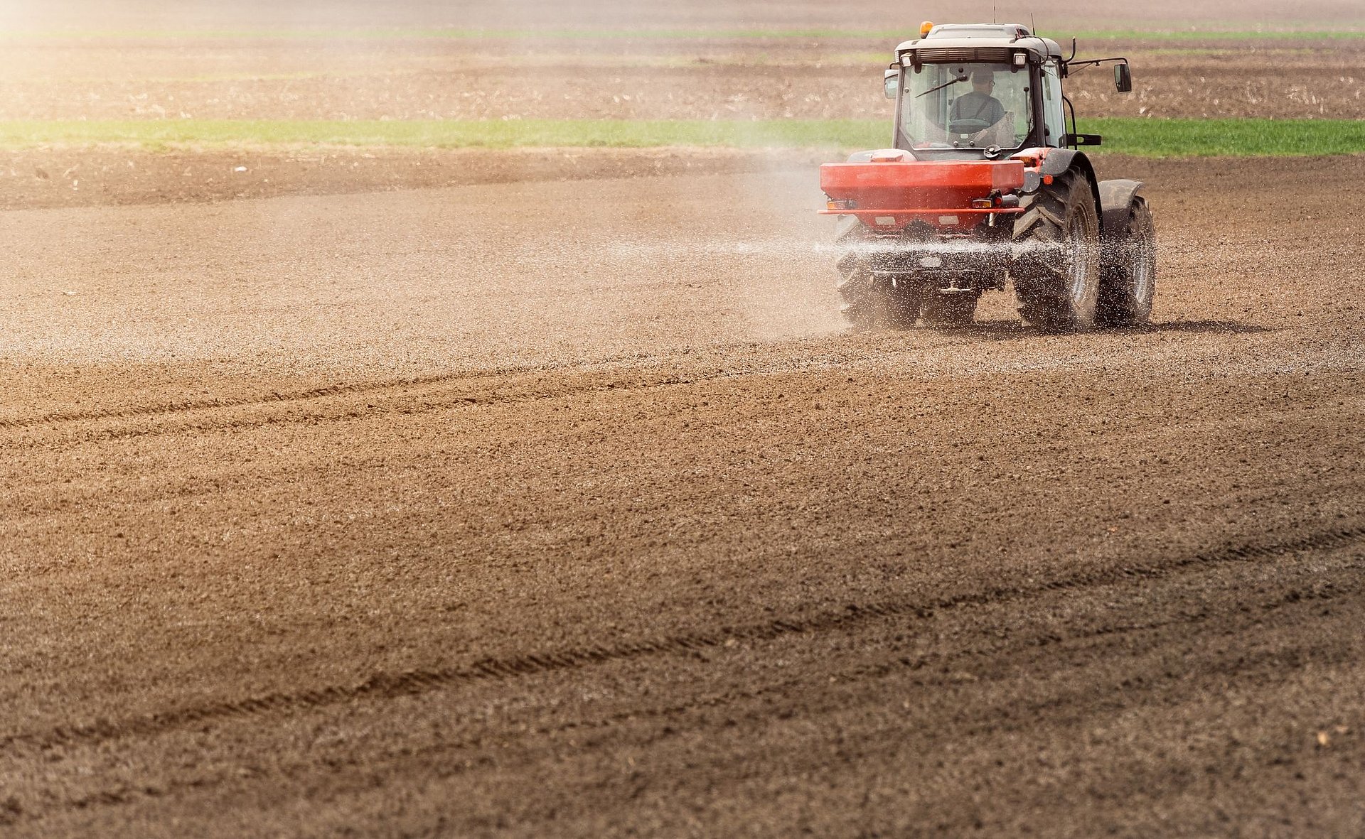 A tractor drives over a field and applies nitrogen fertilizer in a spray mist.