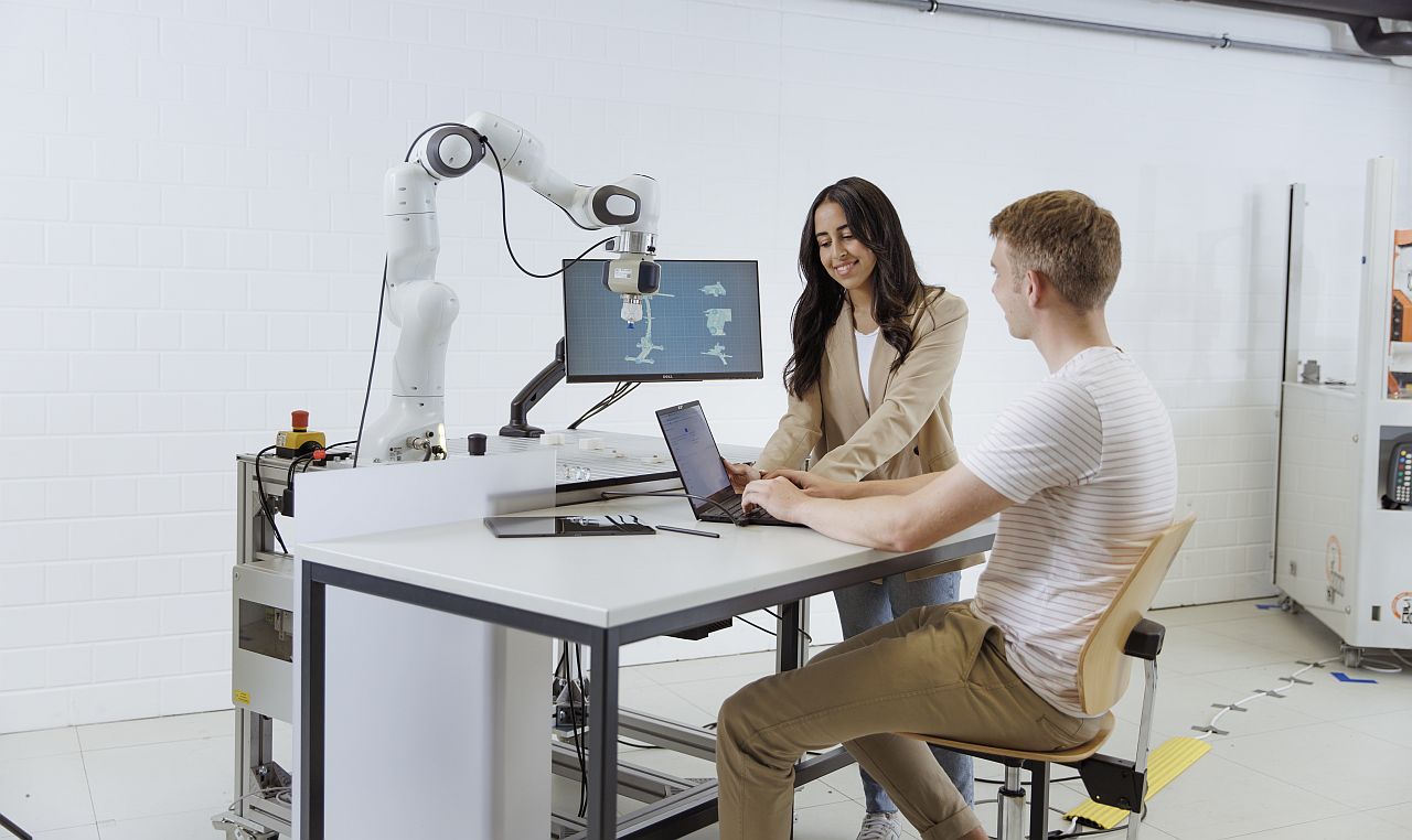 Studierende arbeiten mit Rechner und Roboterarm.