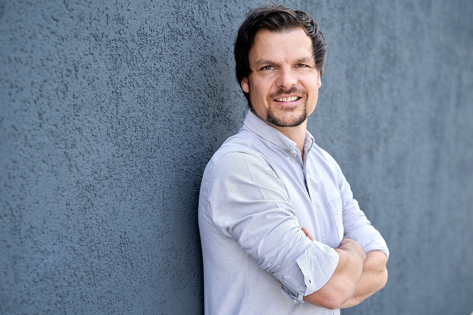 Man with rolled-up shirt sleeves and arms crossed looks into the camera