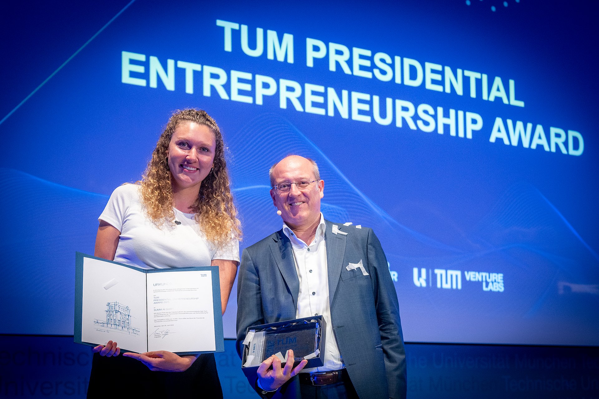 Vice President Prof. Gerhard Kramer presents the TUM Presidential Entrepreneurship Award to Flora Geske, founder of the start-up SUMM AI.