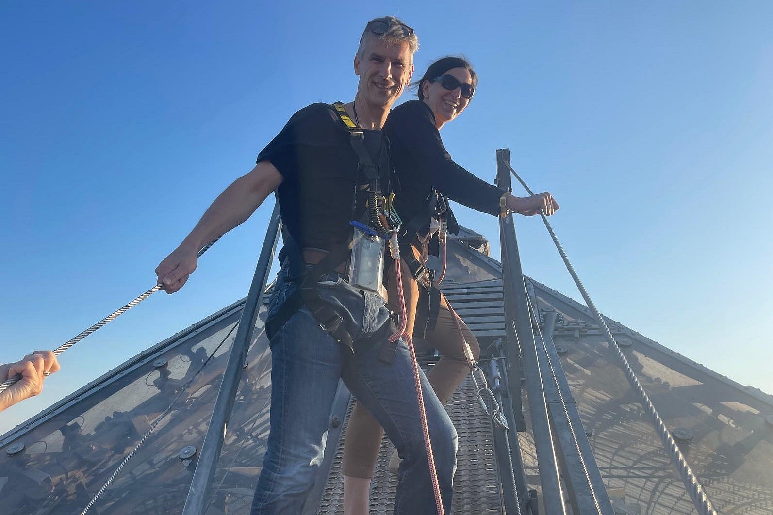 A pair of sponsors stand roped together on the roof of the Olympic tent and smile warmly at the camera.